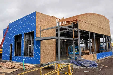 AFCU Rexburg branch under construction — wood framing on blue WRB-wrapped exterior, steel structural frame, and the building's signature curved arc roof feature taking shape