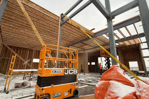 Roof framing in progress at AFCU Rexburg — sloped wood roof structure tied into the steel frame, with a JCB scissor lift staged below