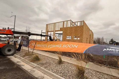 "New Branch Coming Soon" banner at the AFCU Rexburg project site, with the wood-framed building shell visible behind the construction fence