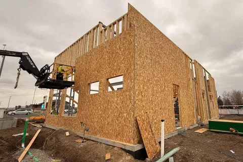 Tall OSB-sheathed end wall at AFCU Rexburg with a man-lift positioned for upper-level framing work
