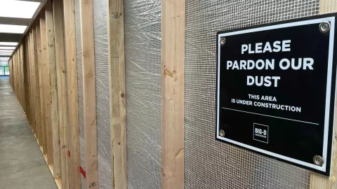 Wood-framed temporary partition wall along the Albion Hall renovation corridor at Idaho State University, with a "Please Pardon Our Dust" sign credited to Big-D Construction