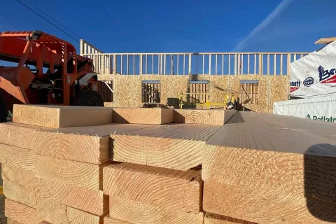 Stack of dimensional lumber in the foreground at the Grand Peaks job site, with framed walls and a telehandler in the background and Bennett Lumber wraps to the side