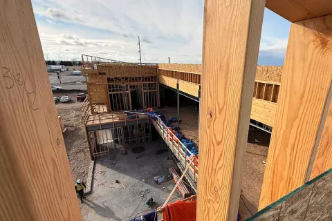 View through wood framing at an upper level of Grand Peaks looking down into the building's courtyard, with framed walls and tarped material below