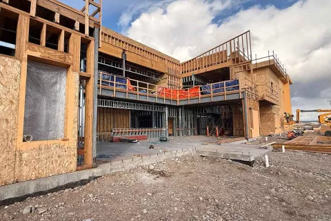Multi-story Grand Peaks building under construction with completed stucco at lower levels, ongoing framing above, and a covered exterior walkway at center