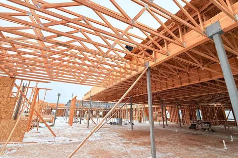 Interior view at Grand Peaks looking up at the engineered roof truss system spanning overhead, with steel columns supporting the structure and snow on the slab