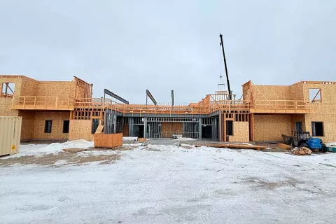 Wide view of the multi-wing Grand Peaks building under construction, with framed second stories on either side of a center bay and a small crane working at the center