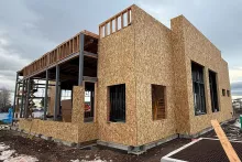 Side elevation of AFCU Rexburg construction showing OSB-sheathed wood framing, steel column-and-beam structure, and recessed window openings