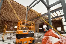 Roof framing in progress at AFCU Rexburg — sloped wood roof structure tied into the steel frame, with a JCB scissor lift staged below