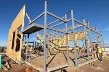 Steel-and-wood structural frame at AFCU Rexburg under clear blue skies, BLU-D crew working on wall framing on the exposed concrete slab
