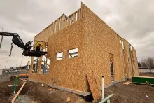 Tall OSB-sheathed end wall at AFCU Rexburg with a man-lift positioned for upper-level framing work