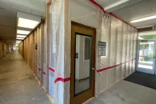 Albion Hall interior corridor during renovation, with wood-framed temporary walls wrapped in plastic sheeting and a "Notice — Construction Area Closed to Public" sign on a doorway