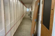 Long Albion Hall hallway during renovation with plastic-sheeted temporary partition walls along one side and a wood door propped against the opposite wall