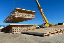 Mountain Crane lifting a prefabricated wood truss section into place at the Alpine Hotel site, with a BLU-D crew member spotting from the ground
