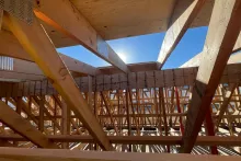 Underside view of engineered roof trusses at the Alpine Hotel showing dimensional lumber, gusset plates, and an open skylight cutout to blue sky