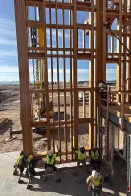 BLU-D crew of six in high-vis hoisting a tall, multi-story wood-framed wall section into position at Grand Peaks, with a telehandler staged behind