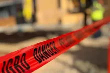 Close-up of red "Danger" safety tape strung across the Grand Peaks job site, with crew members in high-vis softly out of focus behind