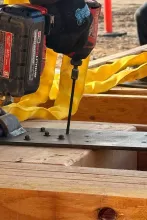 Milwaukee impact driver fastening lag bolts through a steel bearing plate into a heavy timber beam at Grand Peaks