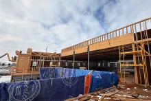 Grand Peaks under construction with a long open-framed second story, scaffolding, and American Builders Supply rental tarps wrapping protected materials