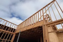 Looking up at the Grand Peaks framed roof structure where wood-framed walls and trusses meet a steel column under a partly cloudy sky