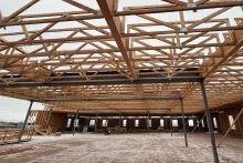 Interior view at Grand Peaks showing engineered roof trusses spanning above steel beams and columns, with the floor below dusted with snow