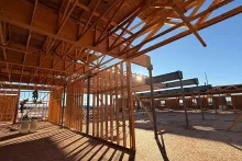 Interior of the Grand Peaks shell with sunlight streaming through wood-framed walls and trusses, steel beams running across, and a framer at work on temporary scaffolding to the left