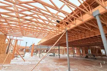 Interior view at Grand Peaks looking up at the engineered roof truss system spanning overhead, with steel columns supporting the structure and snow on the slab