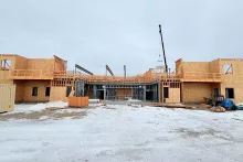 Wide view of the multi-wing Grand Peaks building under construction, with framed second stories on either side of a center bay and a small crane working at the center