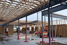 Interior view at Grand Peaks showing the steel beam-and-column grid supporting an engineered roof truss system, with a scissor lift staged below for upper-level work