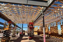 Crew of BLU-D framers on multiple scissor lifts working on the underside of the engineered truss roof at Grand Peaks, with a rich pattern of trusses and gusset plates above