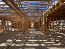 Long second-floor corridor at Alpine Academy, wood-framed classroom walls on both sides under open roof framing, sunlight casting a grid of shadows on the subfloor