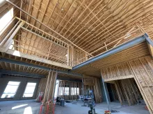 Double-height interior at Alpine Academy: wood roof framing above a framed mezzanine, tied into the structural steel