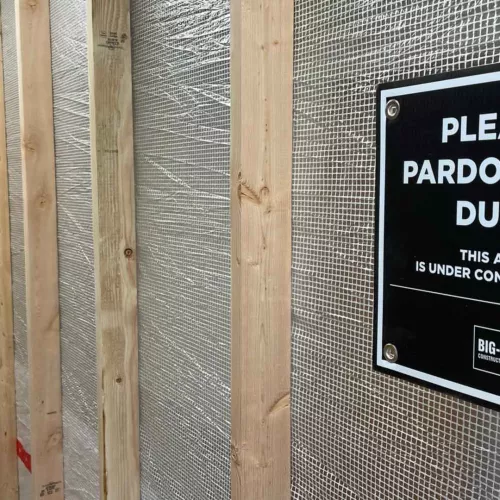 Wood-framed temporary partition wall along the Albion Hall renovation corridor at Idaho State University, with a "Please Pardon Our Dust" sign credited to Big-D Construction